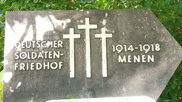 Das Bild zeigt ein Hinweisschild mit drei Kreuzen und der Aufsschrift: "Deutscher Soldaten-Friedhof, 1914-1918, Menen"