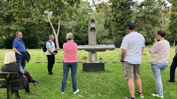 Einige erwachsene Menschen stehen um ein Kunstwerk herum, das am Rande einer Gräberstätte errichtet wurde.