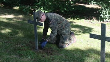 Auf dem Bild sieht man einen Soldaten, die Fundamente eines Grabkreuzes freilegend.