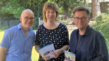 Auf dem Bild sieht man drei Personen, die in die Kamera schauen, zwei Männer und zwei Frauen. In der Mitte steht Astrid Wolters mit einem Faltblatt in der Hand. Links von ihr Stefan Schmidt, rechts von ihr Thomas Kutschaty. Alle drei schauen freundlich.